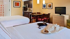 Habitación de hotel con dos camas, zona de comedor, televisor y escritorio.