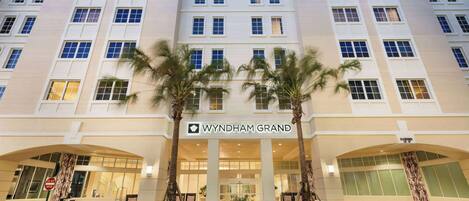 A multi-story hotel with a central entrance, palm trees, and a sign reading "WYNDHAM GRAND".