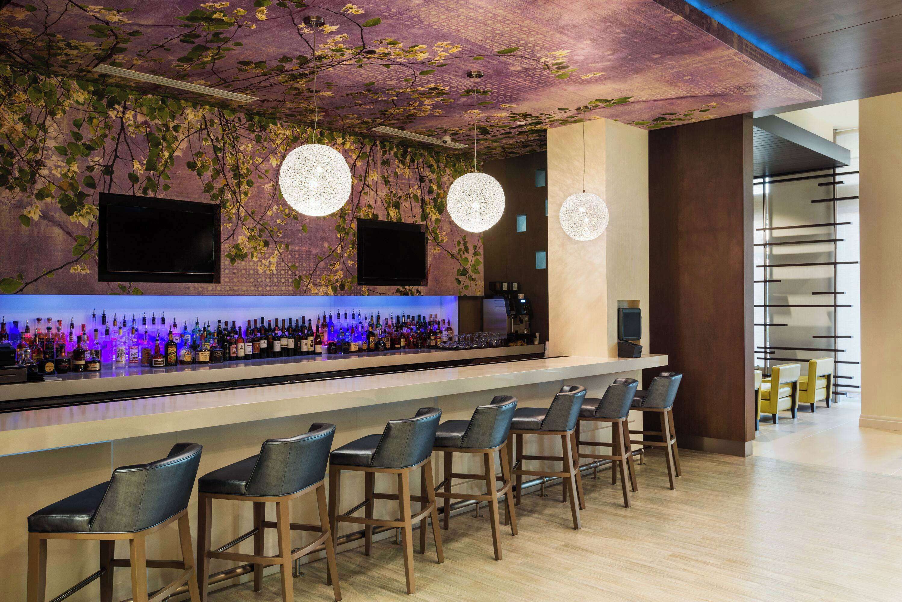 A bar area with a long counter, multiple bar stools, and a television screen.