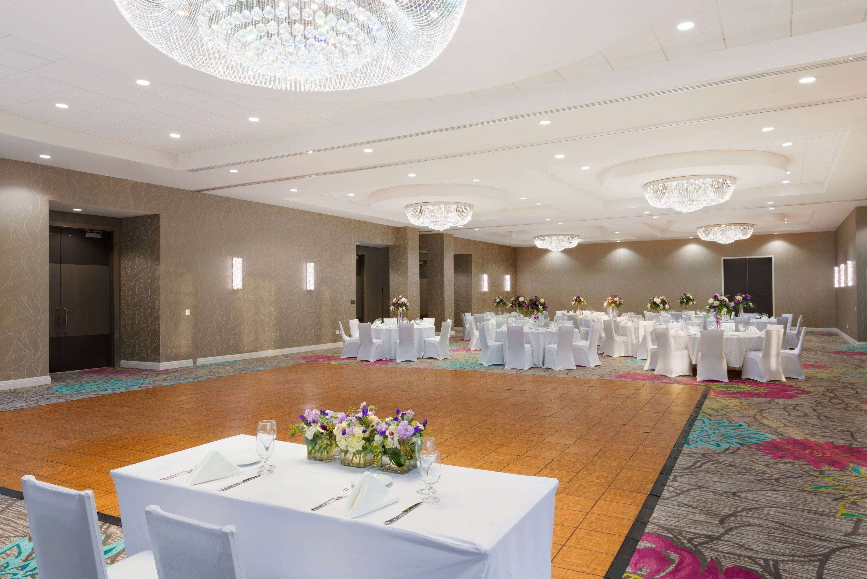 A banquet hall with round tables set for events, chandeliers, and a carpeted floor.