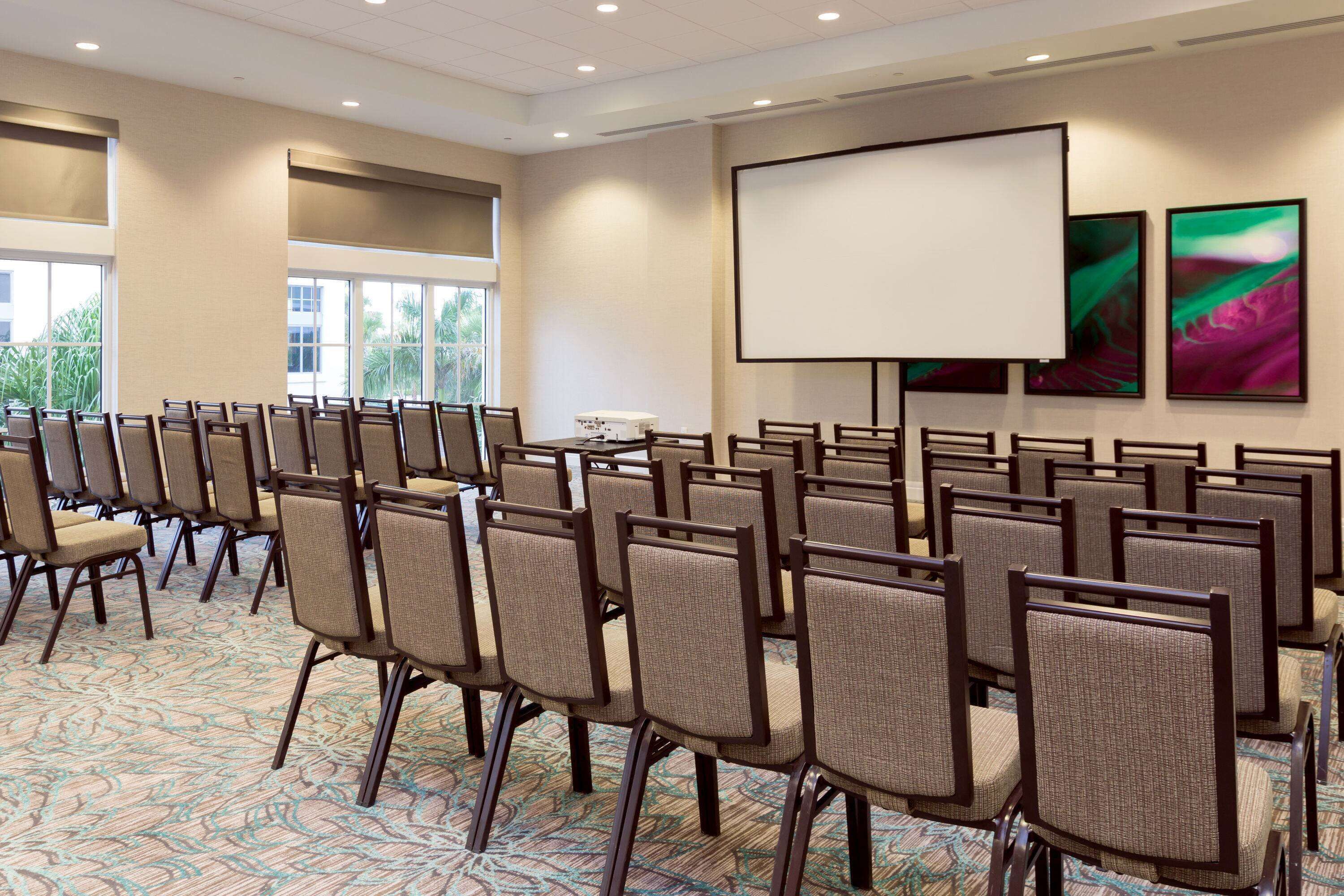 A conference room with rows of chairs, a projector screen, and large windows.