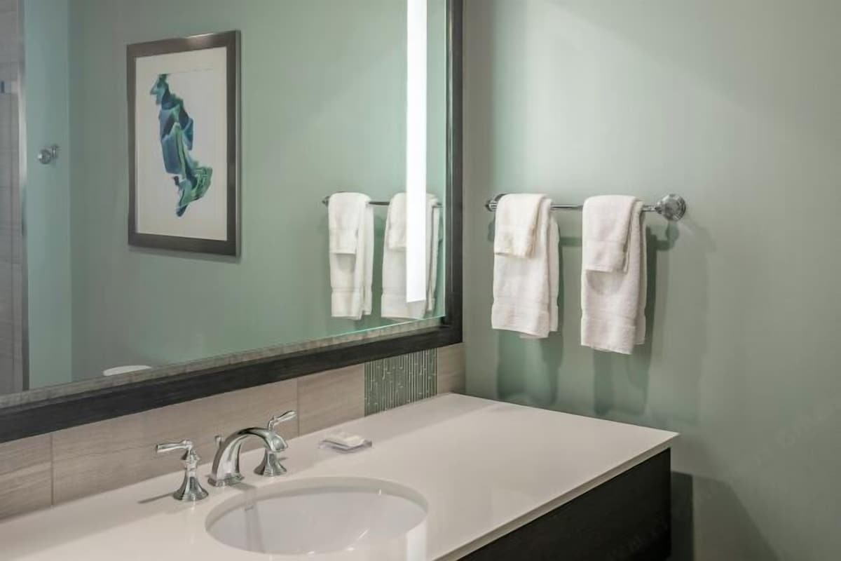 Une salle de bain avec un grand miroir, un lavabo blanc, deux robinets et deux serviettes suspendues à des porte-serviettes.