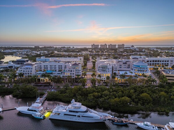 Un hotel frente al agua con varias edificaciones, un puerto deportivo con yates y un horizonte urbano al atardecer.