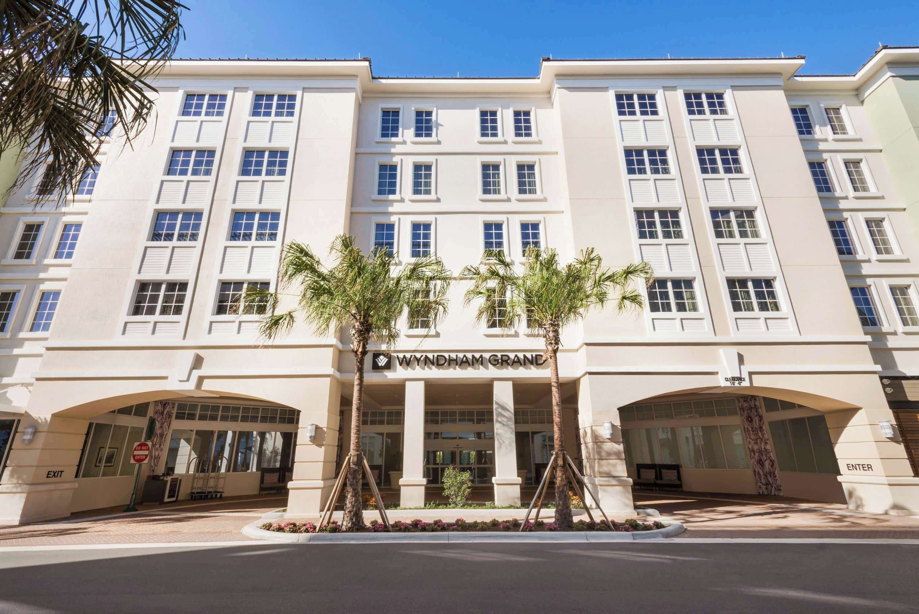 A multi-story hotel with a symmetrical facade, featuring a central entrance with palm trees and an archway.