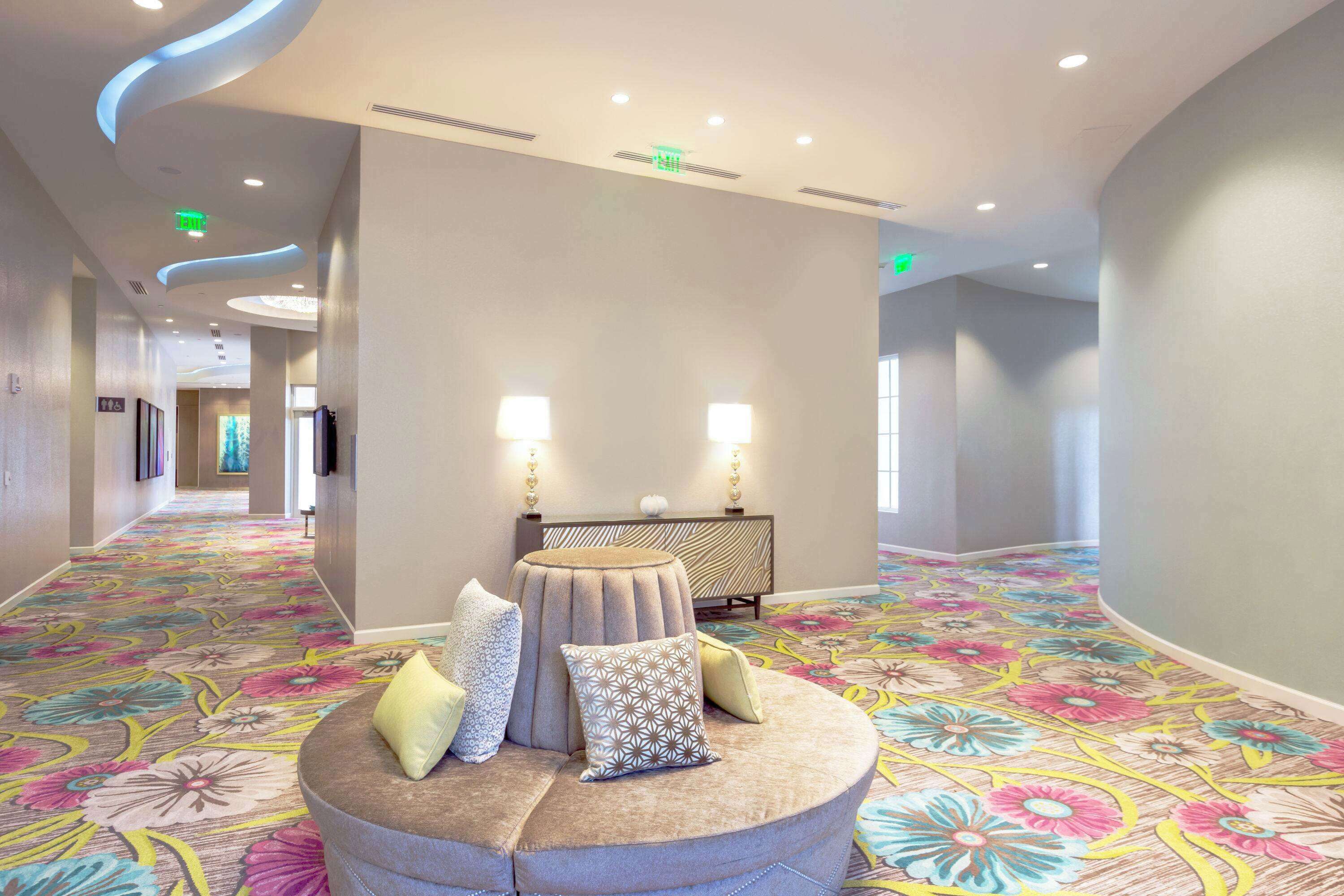 A hotel lobby with a round seating area, a patterned carpet, and a modern ceiling design.