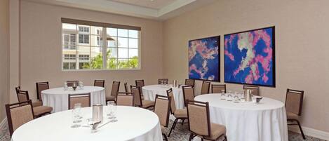 A conference room with multiple round tables, chairs, and a large window with a view of buildings.