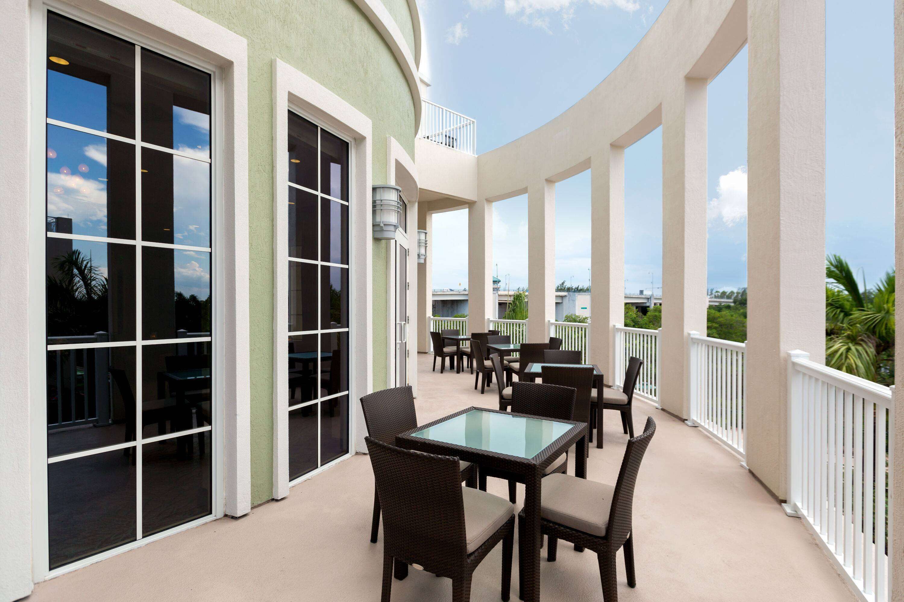 A covered outdoor patio with tables and chairs, large windows, and a view of the surrounding area.