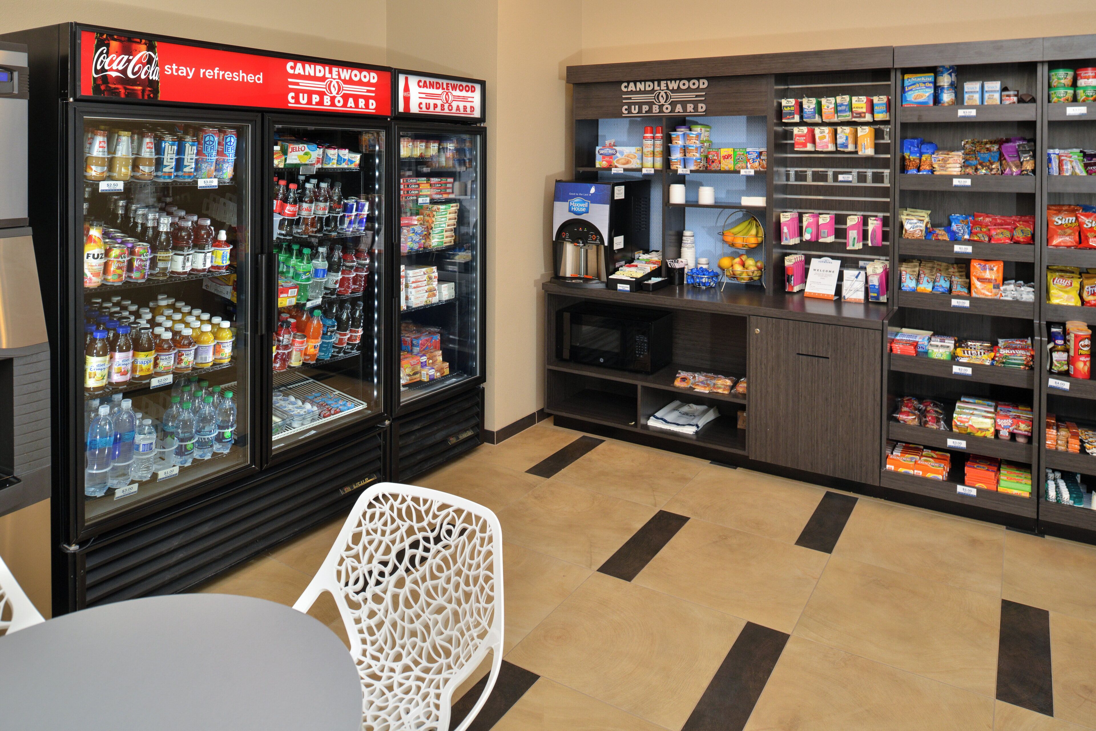 Un espace de vente proposant des distributeurs automatiques aux couleurs de Coca-Cola et de Candlewood Cupboard, ainsi qu'une étagère remplie de divers produits d'épicerie.