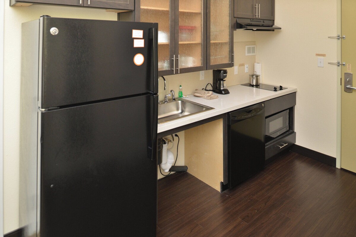Una cocina compacta con un refrigerador negro, un horno empotrado y un microondas.