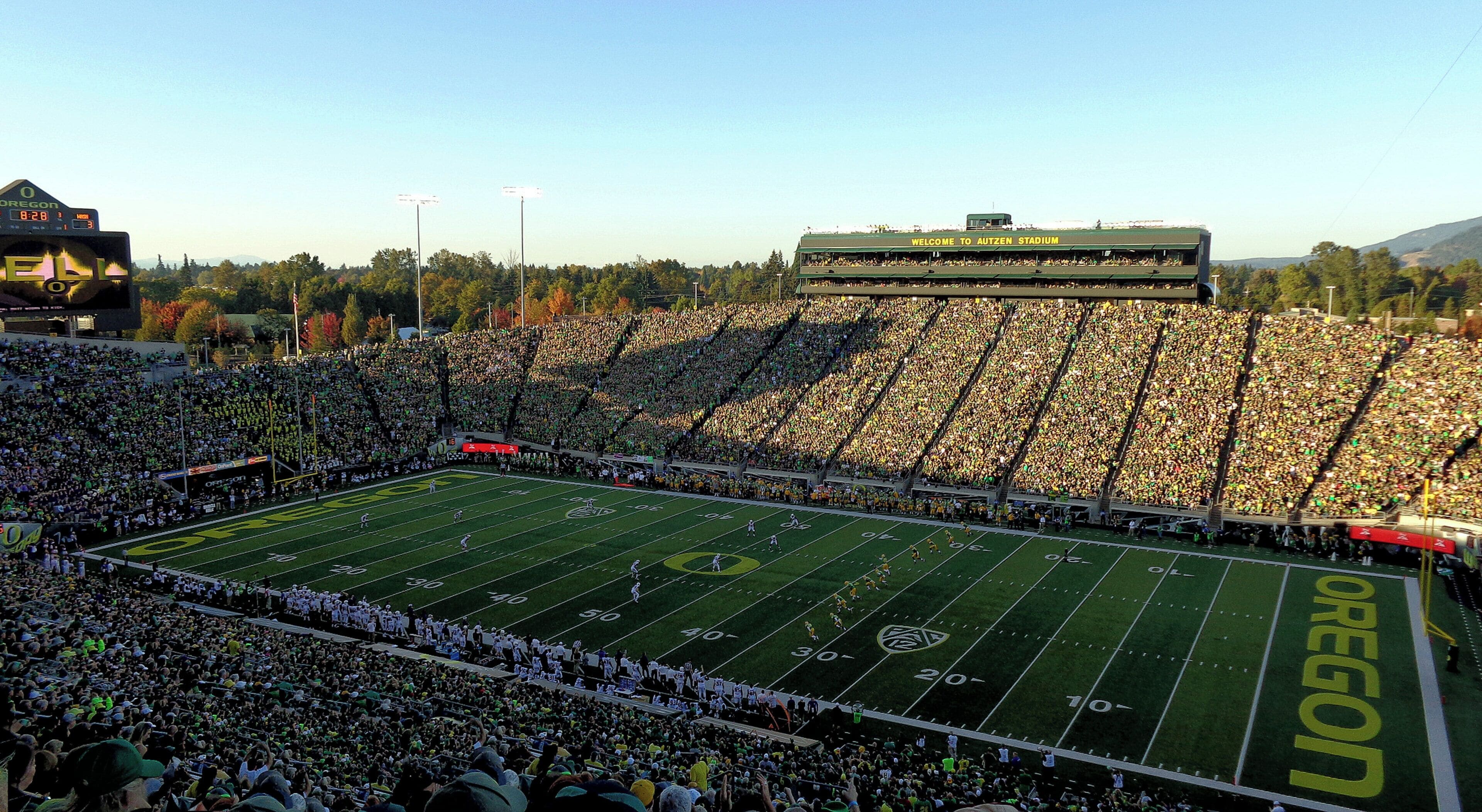 Un estadio de fútbol con una gran multitud, un marcador y la palabra 'Oregon' en el campo.