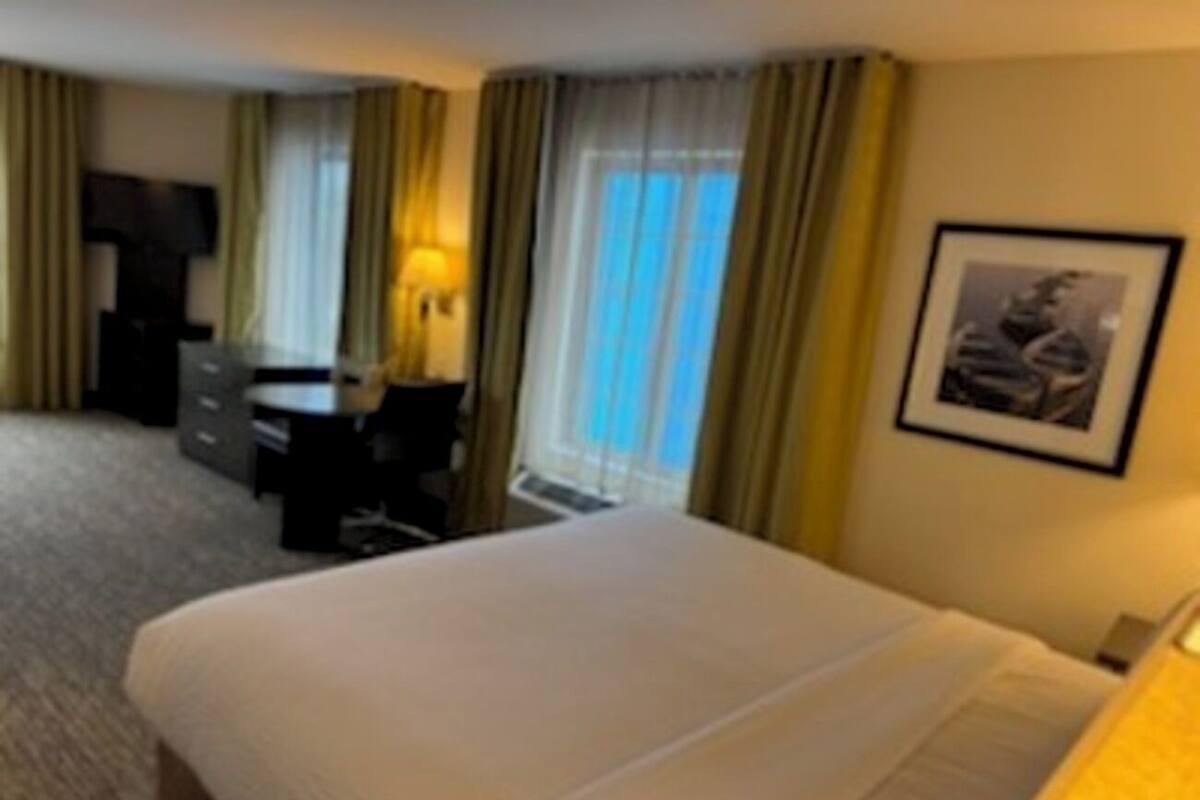 Habitación de hotel con una cama grande, un escritorio y una silla. Hay una ventana con cortinas y un cuadro en la pared.