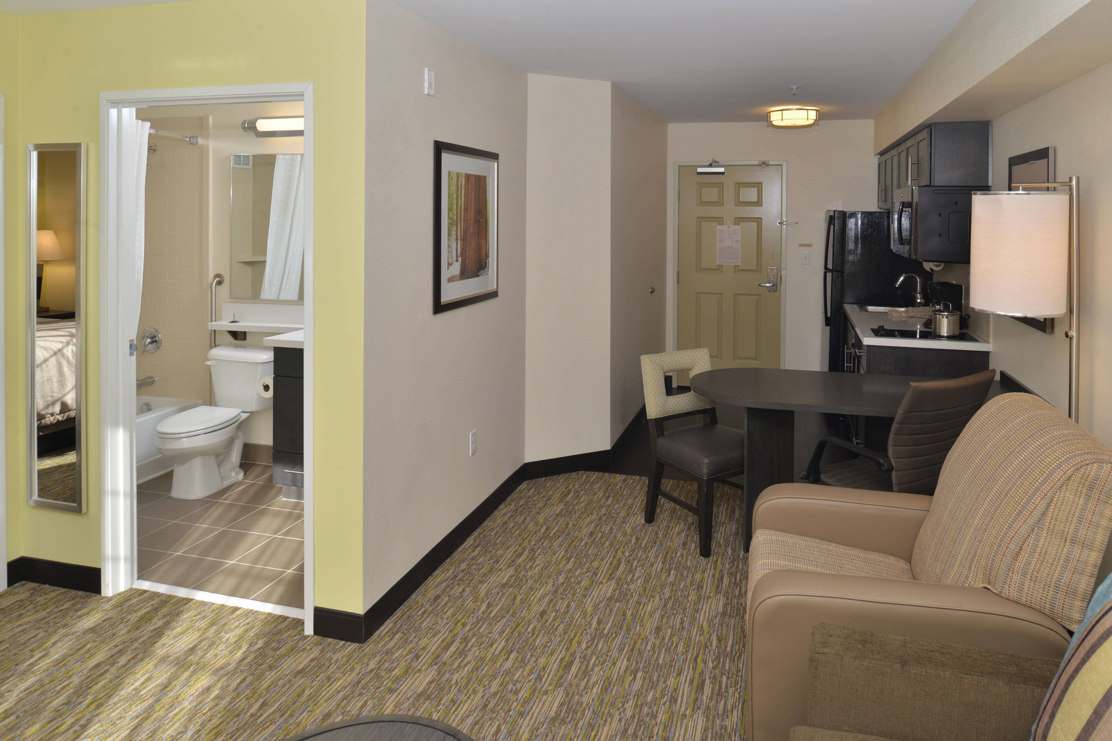 A hotel room with a bathroom, a dining area, and a kitchenette.