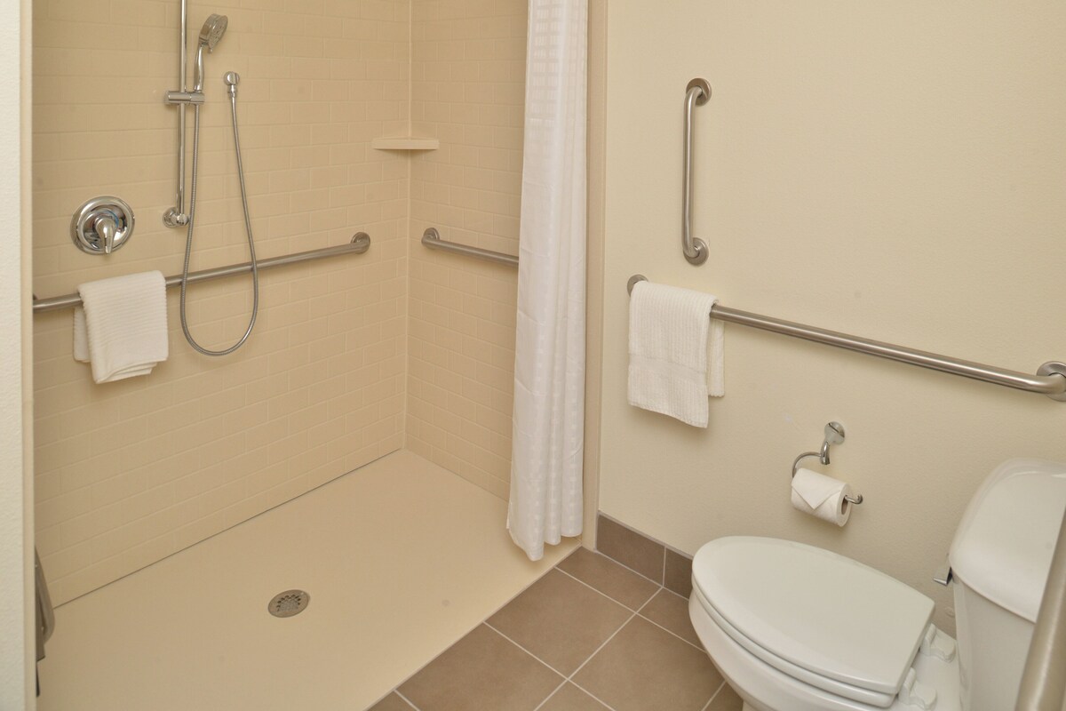 Un baño con ducha, barras de apoyo, inodoro y perchero para toallas.