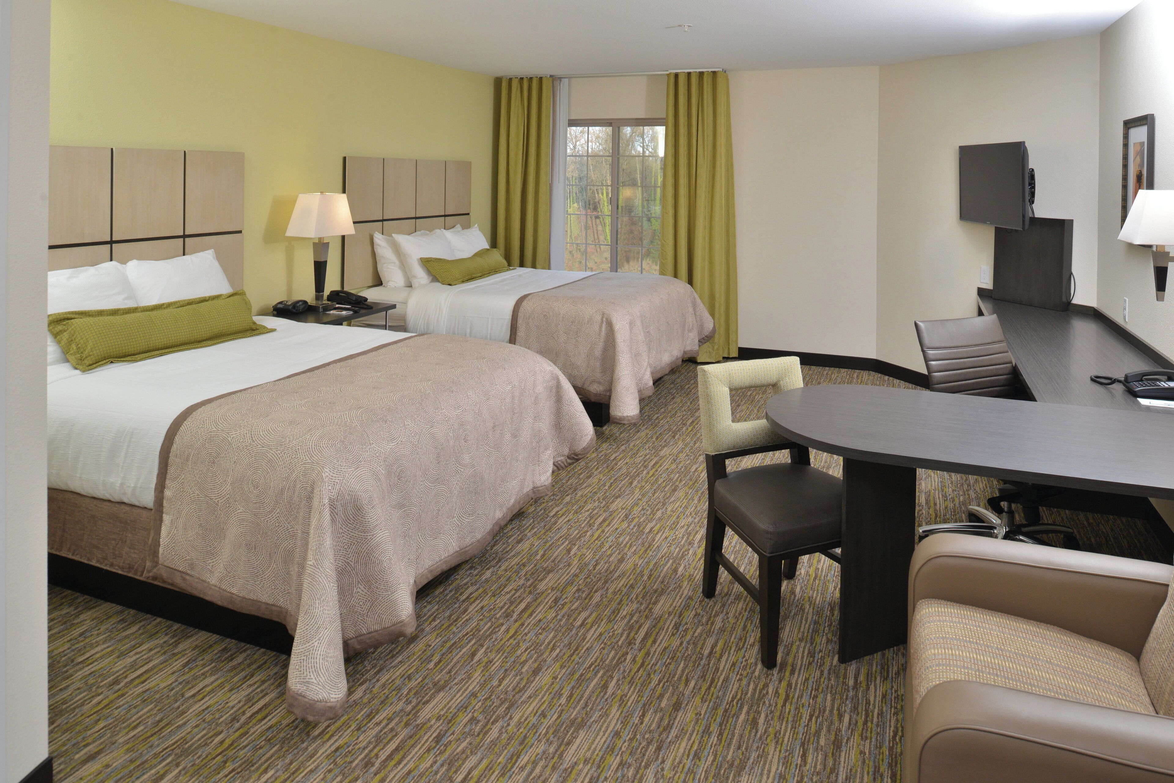 A hotel room with two beds, a desk, a chair, and a television.