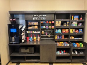 Un quiosco de autoservicio con cafetera, microondas y una variedad de bocadillos y bebidas.