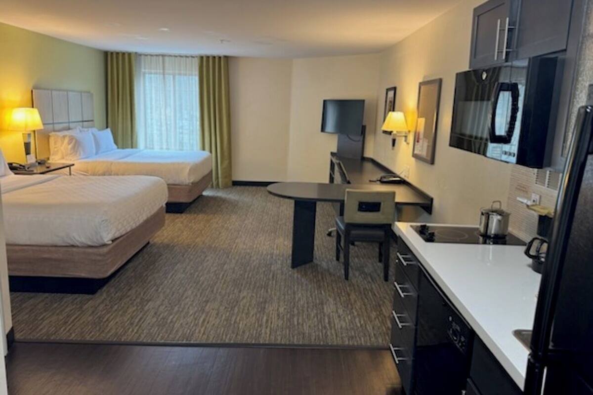 Habitación de hotel con dos camas, un escritorio, una silla, un televisor y una kitchenette.