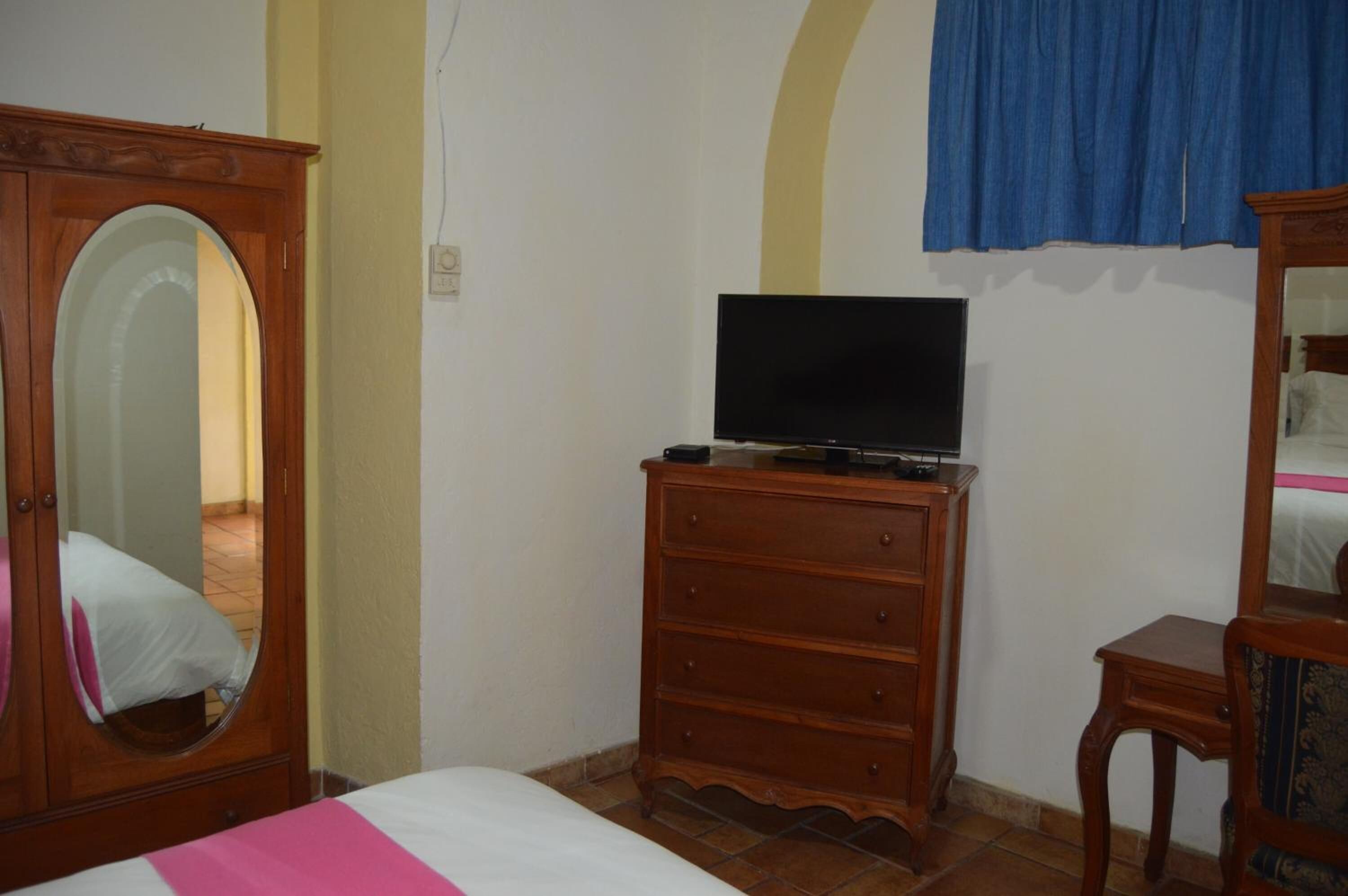 Un dormitorio con cama, cómoda, televisor encima y espejo.