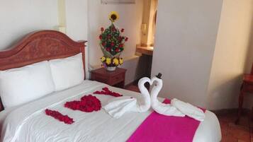 Habitació d'hotel amb un llit ben fet, un ram de flors i una disposició de tovallola amb forma de cigne.