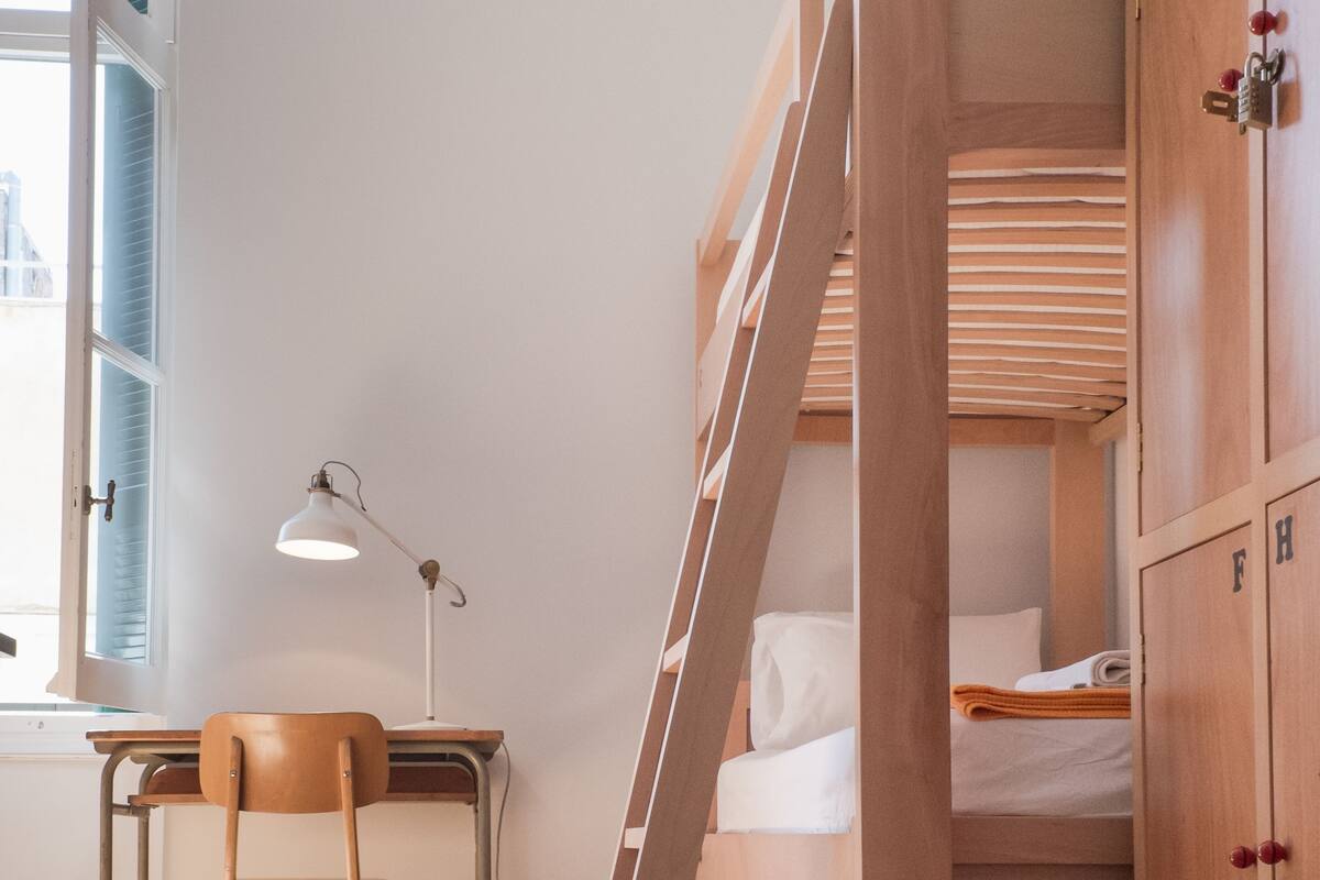 Un lit superposé avec une échelle, un bureau avec une chaise et une lampe de bureau.