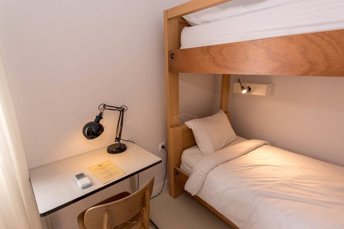 Une chambre avec un lit superposé, un bureau et une chaise, une lampe et une petite étagère.