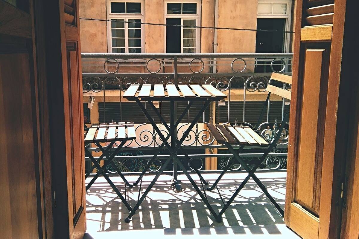 Un balcon doté d’une rambarde en métal et de deux tables en bois.