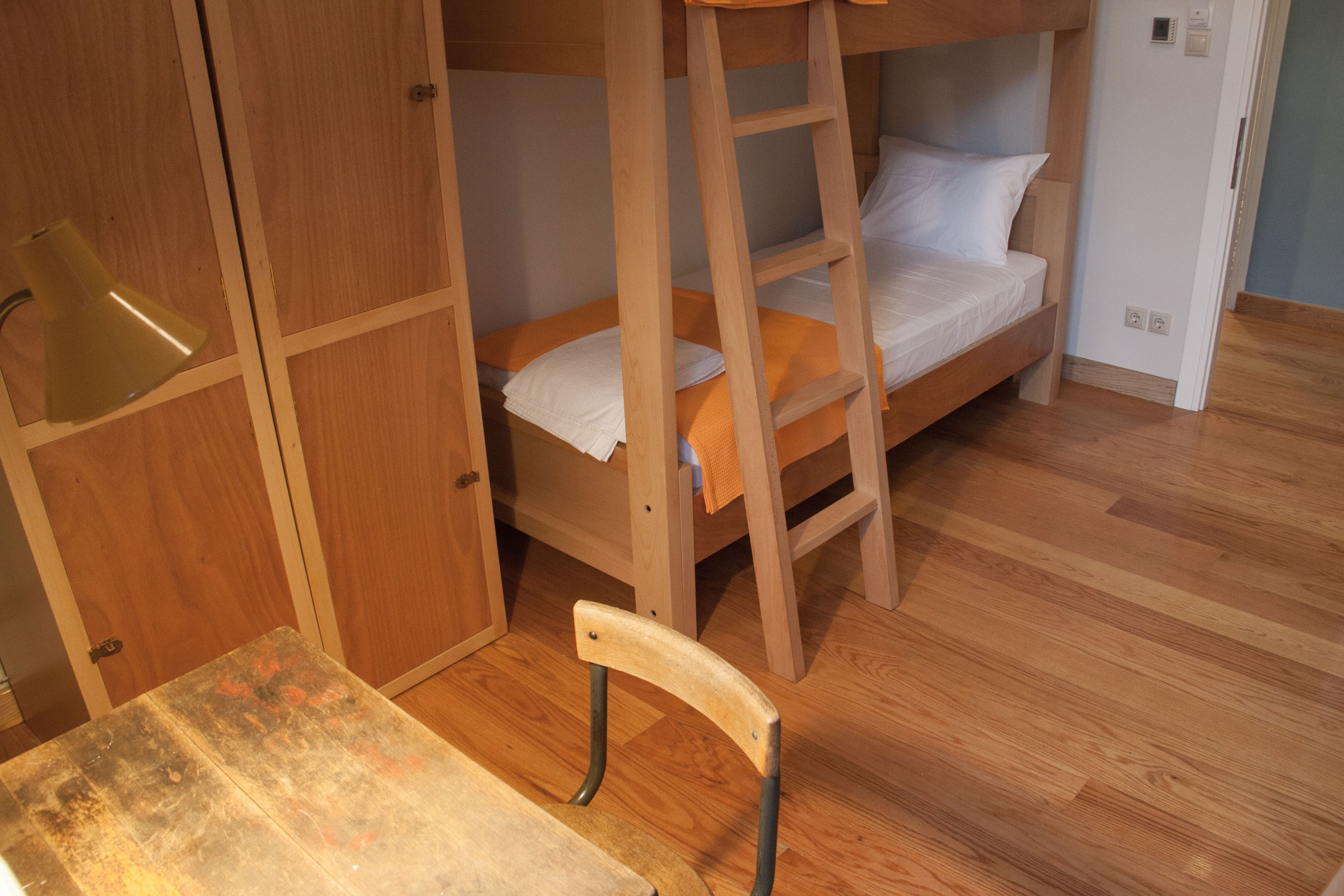 Una cama litera con escalera, una silla de madera y un escritorio en una habitación con suelo y paredes de madera.