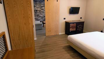 A bedroom with a bed, a dresser, a TV, and a sliding door leading to another room.