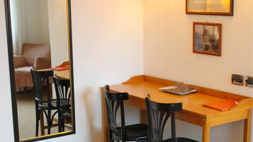 A hotel room with a wooden desk, black chairs, a mirror, and framed pictures on the wall.