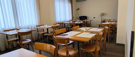 A dining area with multiple tables and chairs, arranged in a spacious room with large windows and curtains.