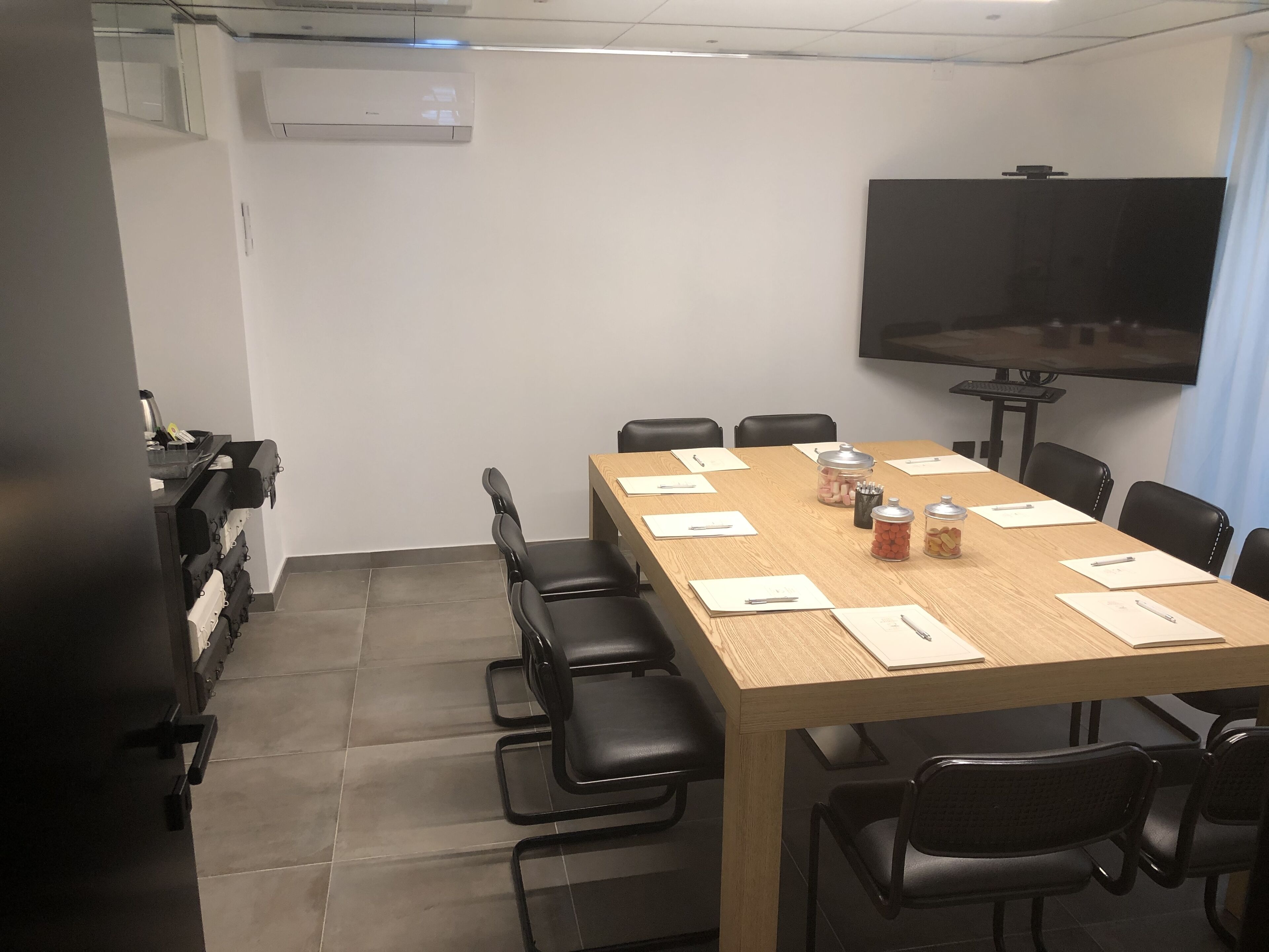 Une salle de conférence avec une longue table, des chaises noires, un écran de télévision et une fenêtre avec des rideaux.