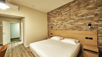 Un dormitorio con cabecera de madera, una cama grande con ropa de cama blanca, una mesita de noche de madera y una pared con estampado de ladrillo.