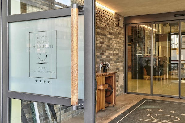 A hotel entrance with a framed sign, a wooden column, a brick wall, and a glass door leading inside.