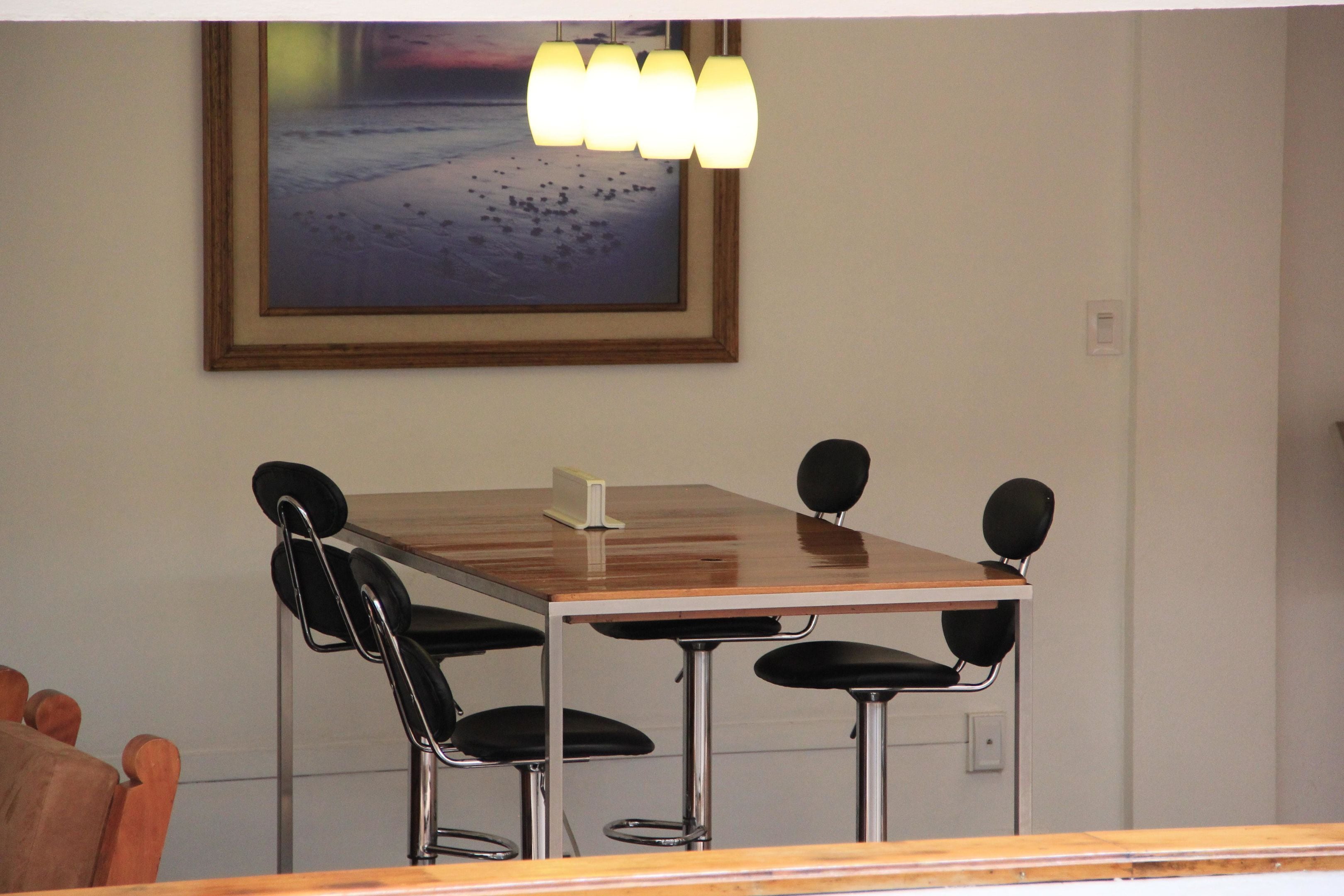 Un salón de conferencias con una mesa de madera, cuatro sillas y un cuadro en la pared.