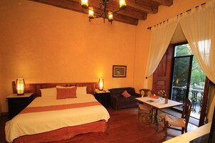 Une chambre d’hôtel comprenant un lit, une table de chevet, une table avec des chaises, un canapé et une fenêtre avec des rideaux.
