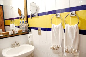 Un baño con un lavamanos blanco, dos espejos y toallas colgadas en barras.