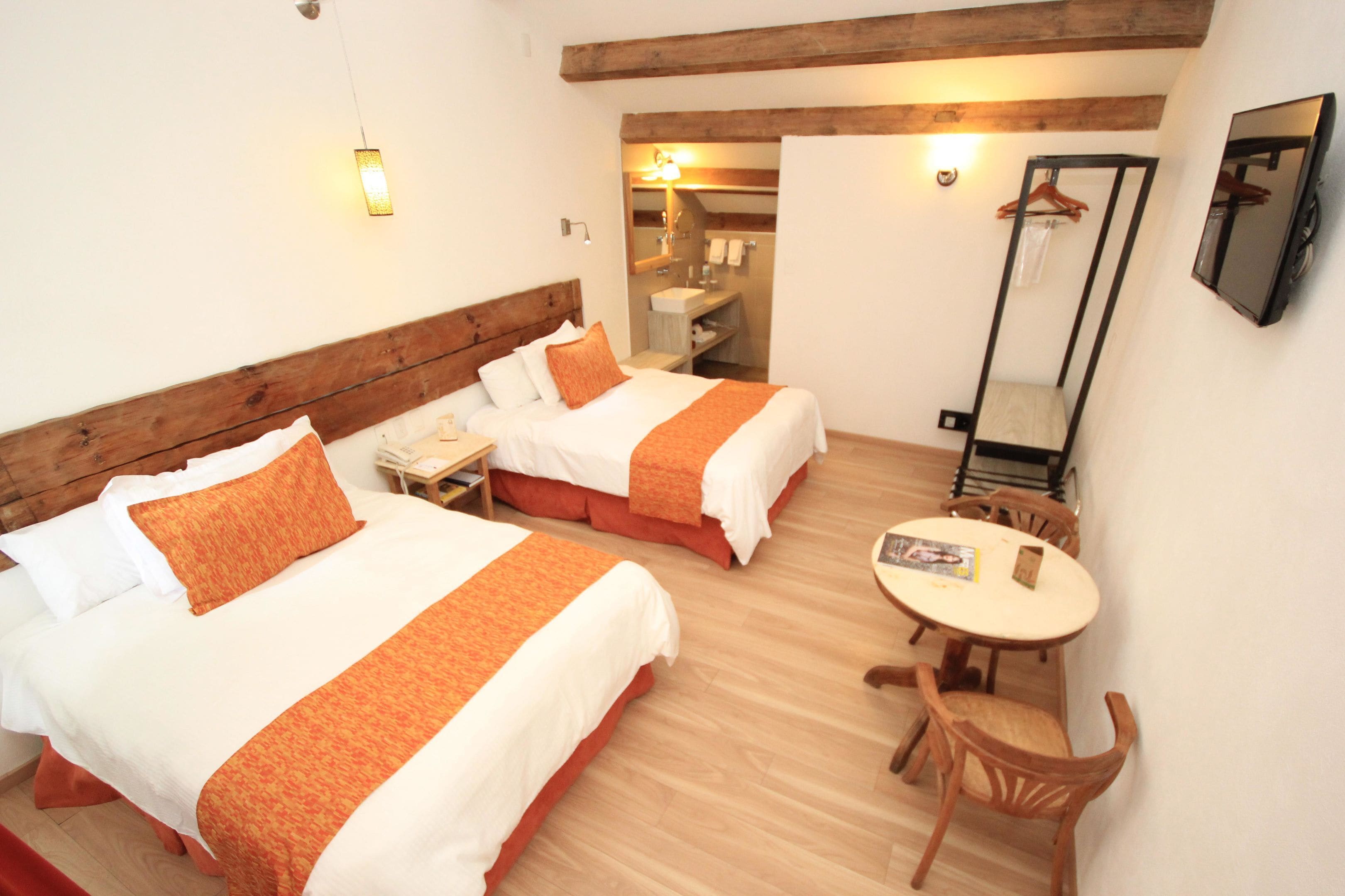 A hotel room with two beds, a small table, a chair, a mirror, and a bathroom visible through an open door.