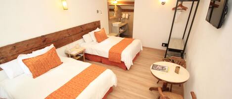 A hotel room with two beds, a small table, a chair, a mirror, and a bathroom visible through an open door.