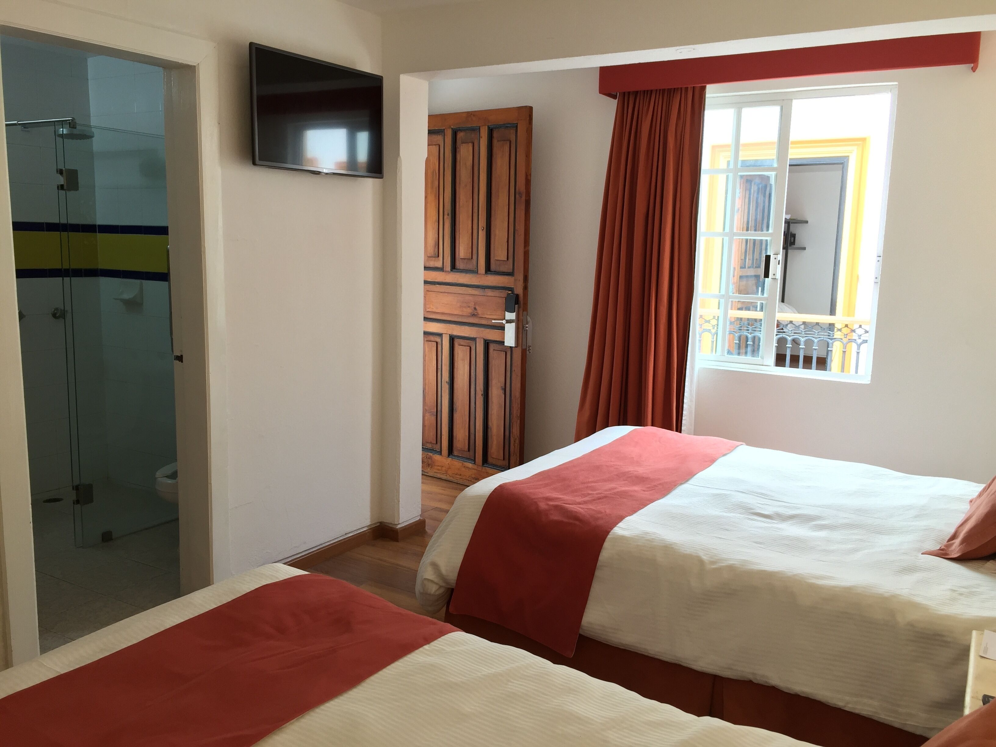 Een hotelkamer met twee bedden, een televisie, een houten kledingkast en een raam met gordijnen.