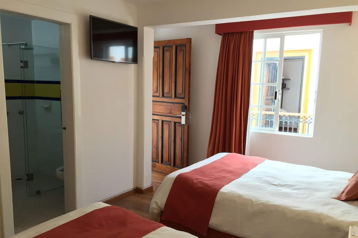 Une chambre d’hôtel avec deux lits, une télévision, une armoire en bois et une fenêtre avec des rideaux.