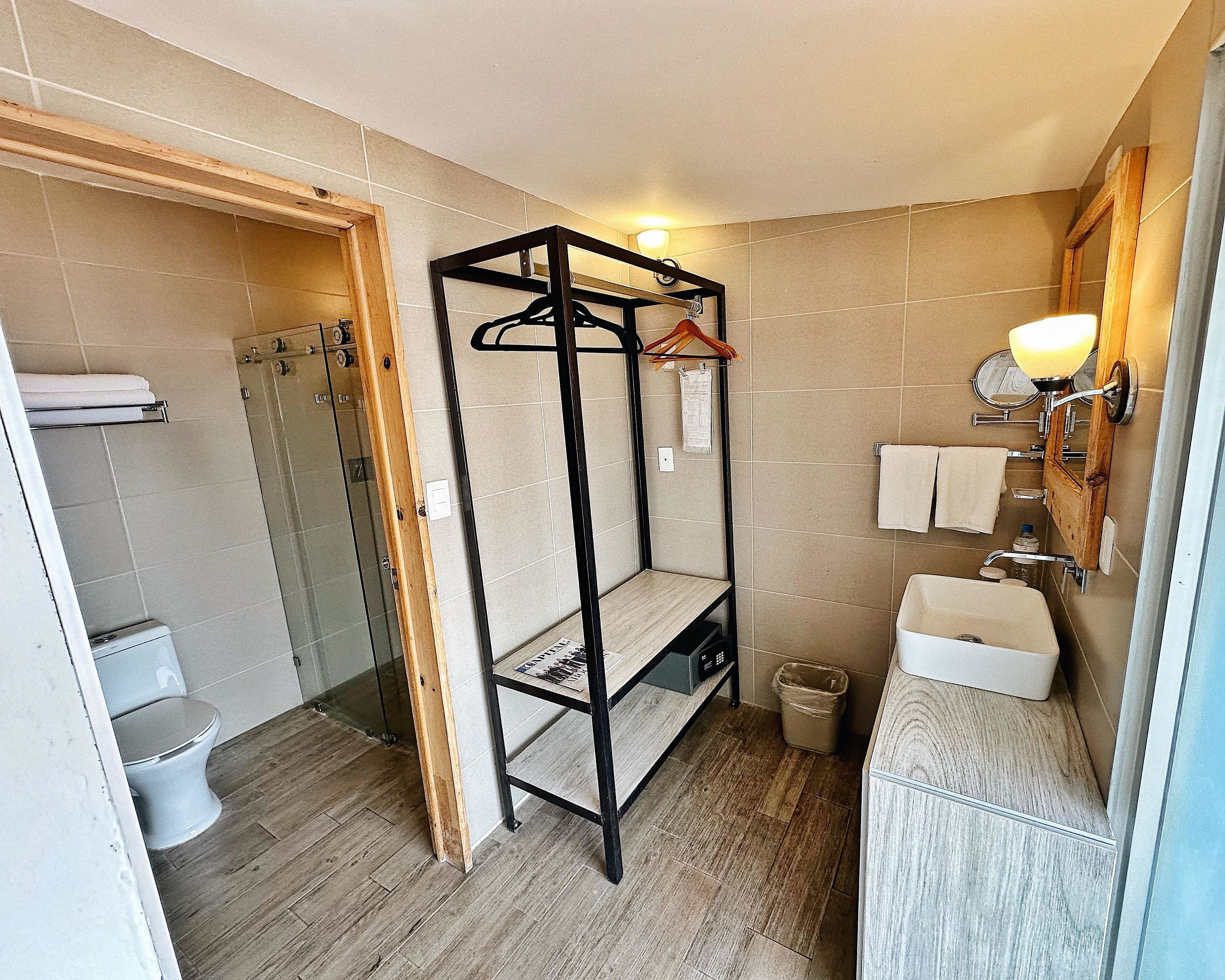 A bathroom with a shower, toilet, and a wooden shelf unit with a towel rack.