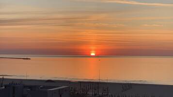 Un coucher de soleil sur une mer calme, avec une plage au premier plan.