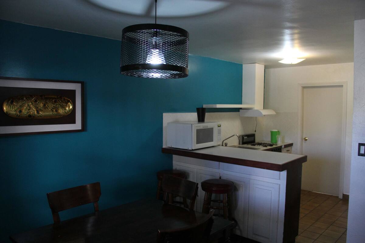 A compact kitchen with teal walls, a white microwave, and a hanging light fixture.