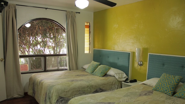 Una habitación con dos camas, una ventana con cortinas y una pared amarilla.