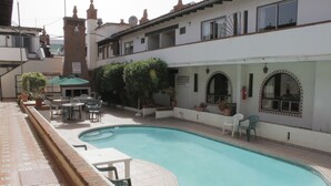 Una piscina con cubierta de baldosas, mobiliario exterior y plantas en macetas.