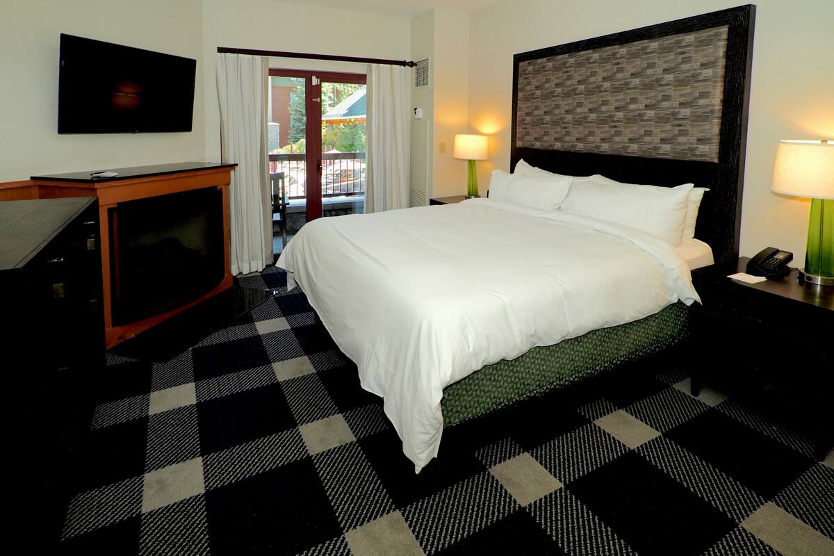 A hotel room with a large bed, a television, a desk, and a balcony with a view.