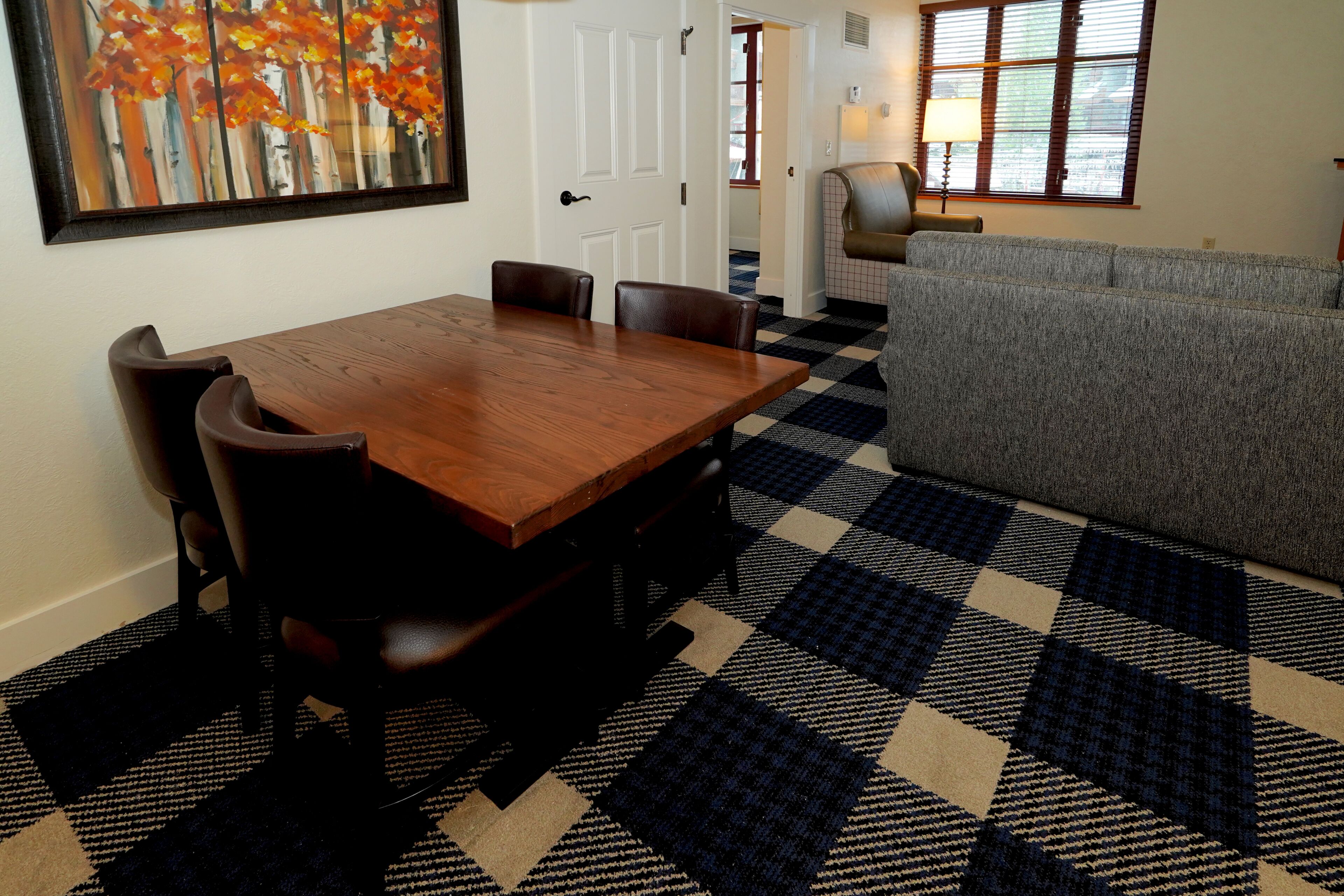 A dining area with a wooden table and chairs, a patterned rug, and a gray sofa.