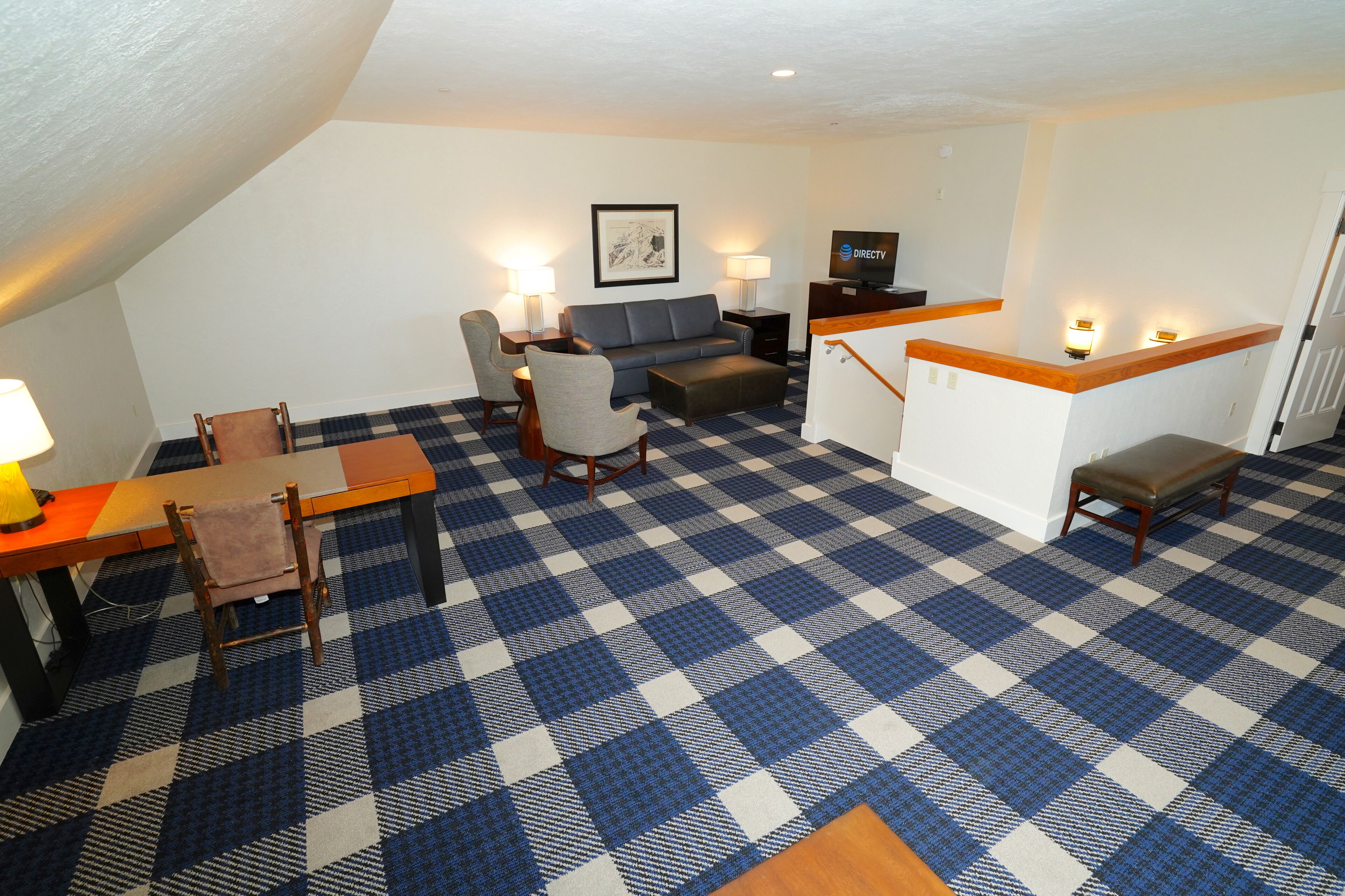 Ein Hotelzimmer mit Schachbrettmuster-Boden, einer Couch, einem Esstisch mit Stühlen, einem Fernseher und einer Treppe mit Holzwand.