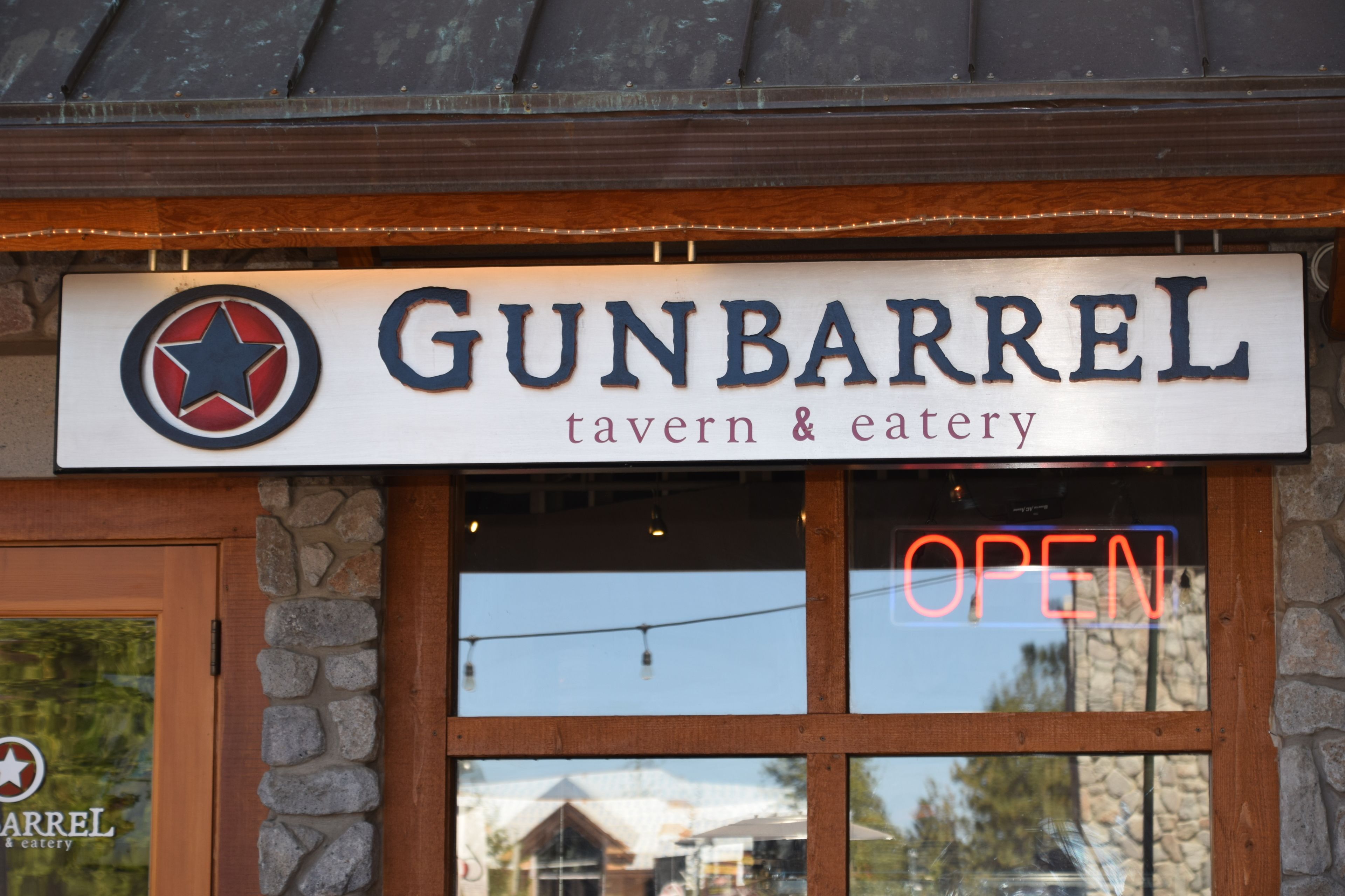 Señal del tabernero y restaurante Gunbarrel, con un letrero de neón que dice 'ABIERTO' sobre la entrada.
