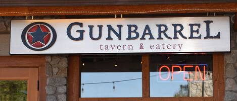 Señal del tabernero y restaurante Gunbarrel, con un letrero de neón que dice 'ABIERTO' sobre la entrada.