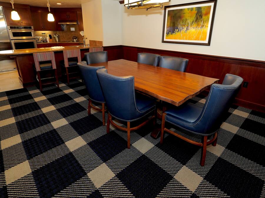 Un coin repas avec un sol à carreaux, une table en bois et des chaises recouvertes d’un tissu bleu.